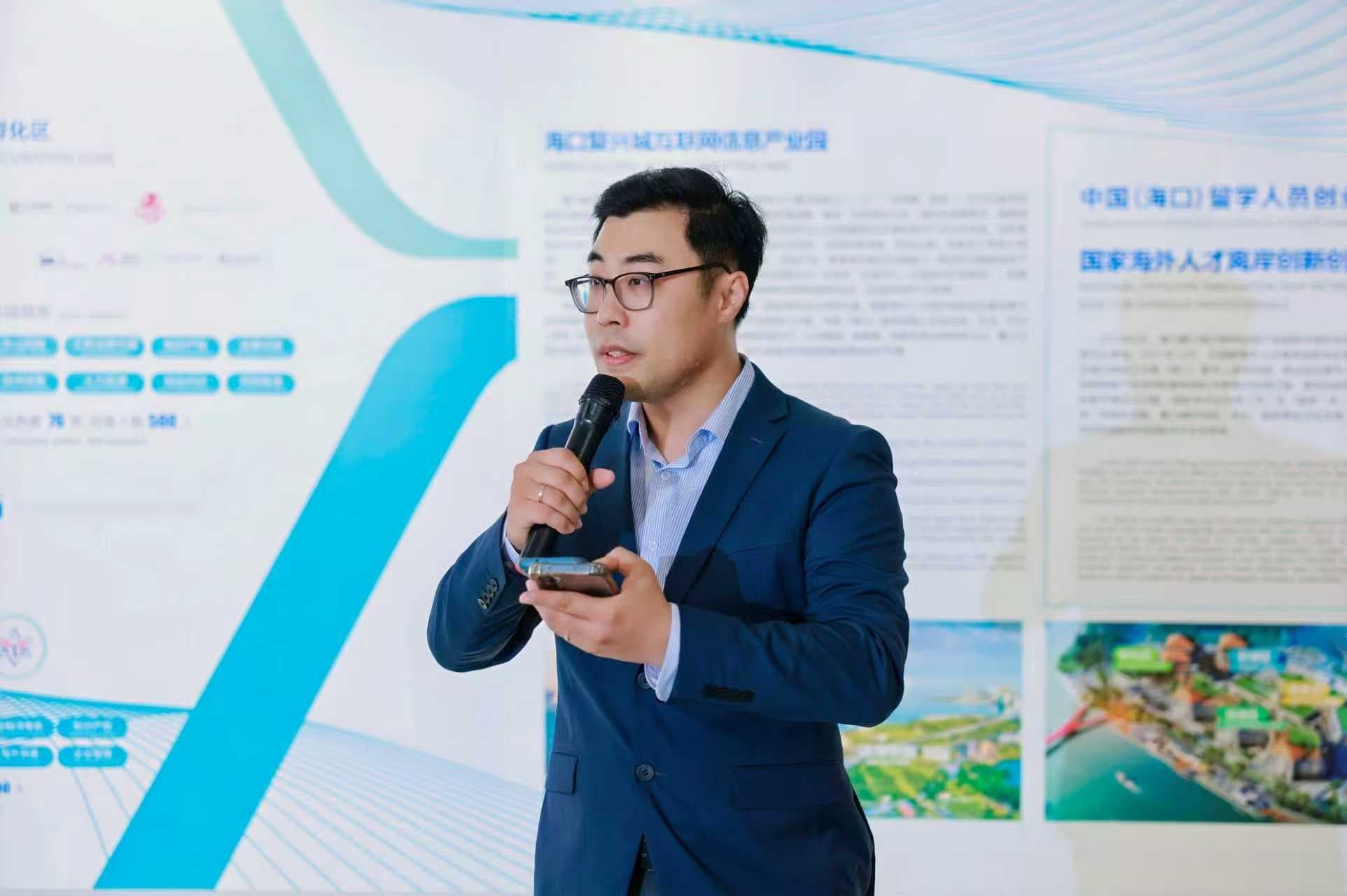 Man in a blue suit and glasses speaking into a microphone while holding a smartphone.