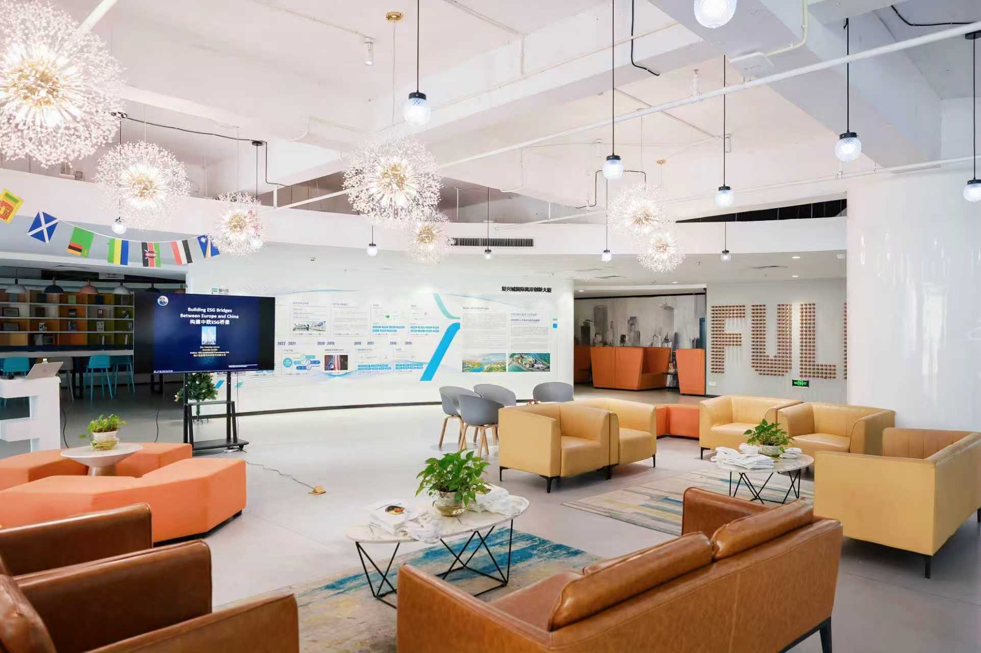 Modern office lounge featuring tan leather seating, dandelion-style pendant lights, and a presentation screen.